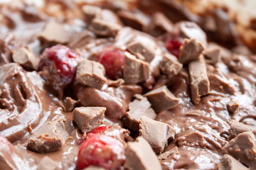 Background of chocolate dough with pieces of milk chocolate and frozen cherries