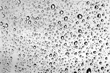 Large raindrops on a window glass in rainy cloudy day against a gray sky. Autumn, depressive, rainy weather. Selective focus. Black and white photo