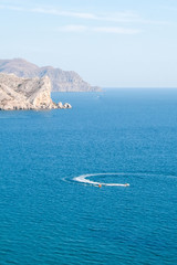 Scenic view of the sea and mountains. Curved trail of a scooter on the water surface