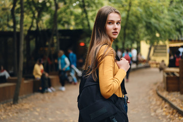Beautiful casual student girl with backpack intently looking in camera in park