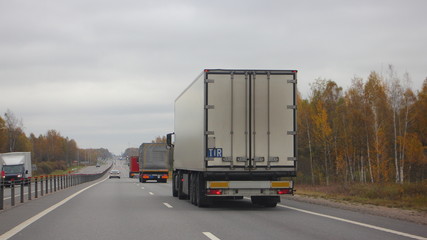 Logistics, shipping goods, road transportation - diesel semi truck with TIR sign (Transports International Routiers) moving on a two-lane asphalted suburban road on autumn day, side rear view