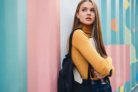 Beautiful pensive student girl with laptop thoughtfully looking away over colorful background