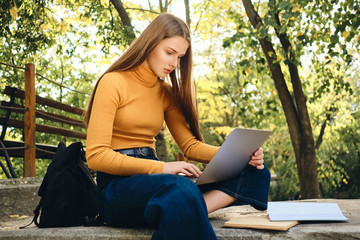 Attractive casual student girl thoughtfully studying on laptop in park