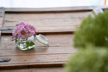 Fototapeta na wymiar Beautiful flowers in glass on wooden shabby furniture with green in foreground