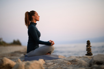 Young woman doing breathing exercise in lotus position at the beach.