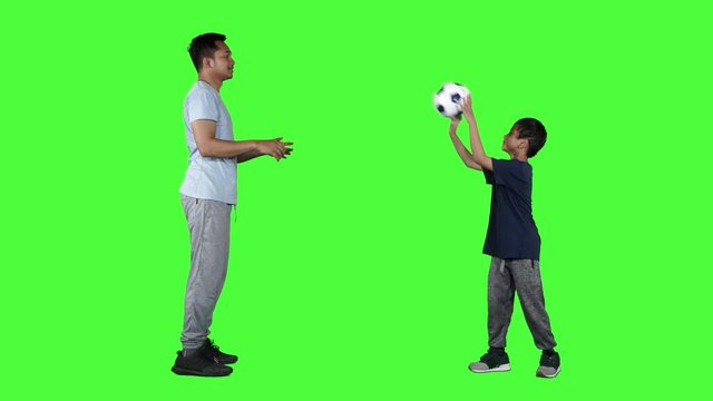 Happy little boy and his father throwing and catching a soccer ball in the studio. Shot in 4k resolution with green screen background