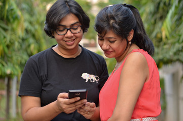 Two friends sitting on a red park bench looking into the mobile phone and smiling and laughing in New Delhi, India