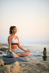 Fototapeta na wymiar Calm woman during meditation exercise on a rock at the beach.