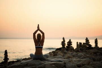 Back view of woman meditating on the beach at sunset.