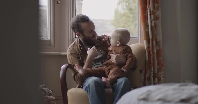 Single father playing with baby boy on chair in bedroom