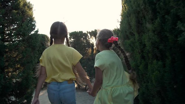 Little girls running in a hedge maze, two sisters kids hold hands and run in big green labyrinth in city park