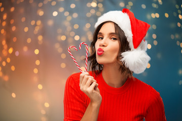 christmas, holidays and people concept - happy smiling young woman in santa helper hat with candy...