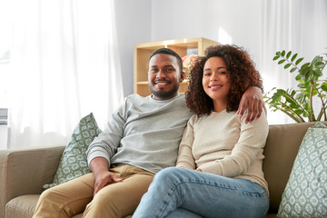 relations and people concept - happy african american couple sitting on sofa and hugging at home