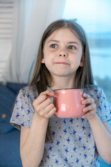 Closeup portrait of a cute little girl with a white milk mustache looking at the camera, pleased charming child with a smile holds a glass, drinks milk before bedtime