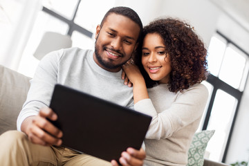 Obraz premium technology, internet and people concept - happy african american couple with tablet computer at home