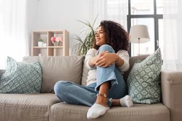 Fotobehang people, race, ethnicity and portrait concept - happy african american young woman sitting on sofa at home © Syda Productions