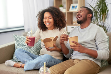 eating and people concept - happy african american couple with takeaway food and drinks at home