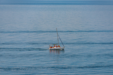 Aerial view on a white floating sailboat with people in it in the blue black sea