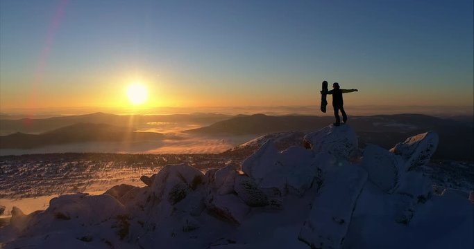 Aerial view. Freerider stands on top of the mountain, snowboard in hand. movable camera plans. Fresh powder. Extreme freeride skiers skiing from the top. beautiful storm of snow flying in the frame
