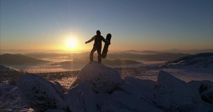 Aerial view. Freerider stands on top of the mountain, snowboard in hand. movable camera plans. Fresh powder. Extreme freeride skiers skiing from the top. beautiful storm of snow flying in the frame