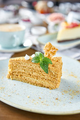 Honey sponge cake decorated with meringue and mint leaves.. Breakfast in the cafe, morning coffee. Cappuccino and lots of desserts on the table.