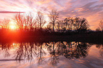 Lake with the reflection of silhouettes of trees on the background of a bright sunset in autumn.