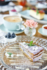 Blueberry sponge cake decorated with meringue and mint leaves.. Breakfast in the cafe, morning coffee. Cappuccino and lots of desserts on the table.