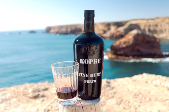 ALGARVE, PORTUGAL: Porto wine tasting on cliff over ocean waves, with bottle of tasty beverage from old winery on 12 May, 2019. Portuguese language has 250 million total speakers