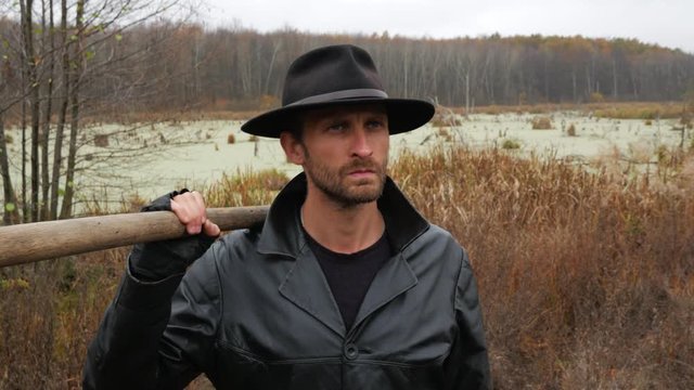 Close-up of a gangster with a shovel on the banks of an old swamp and forest