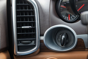 The interior of the car with a view of the dashboard, engine start button and ventilation duct with light brown leather trim