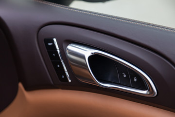 The interior of the car with a view of the dashboard, door handle and memory seat buttons with light brown leather trim