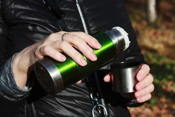 Naklejka premium Woman pours tea from a thermos in the woods