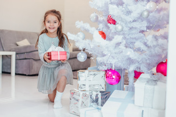 Lovely kid is preparing presents for winter holidays, putting them under the firtree.