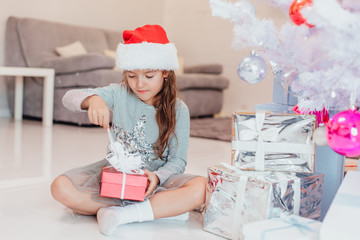 Full-body photo of super excited young girl opening a christmas present while sitting on the floor...