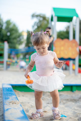 Naklejka premium Cute toddler girl playing in sand on outdoor playground. Beautiful baby in red trousers having fun on sunny warm summer day. Child with colorful sand toys. Healthy active baby outdoors plays games