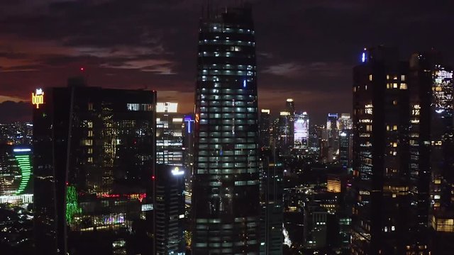 JAKARTA, Indonesia - October 22, 2019: Exotic aerial view of night lights glowing on the silhouette of skyscrapers in business district. Shot in 4k resolution from a drone flying forwards