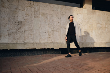 Young handsome man in coat thoughtfully looking away walking outdoor