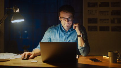 Professional Man Sitting at His Desk in Office Studio Working on a Laptop in the Evening. Man...