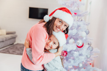 Loving mother and daughter hugging near christmas tree, looking amazing.