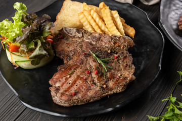 The beef of the cow grilled until cooked served with garlic bread, french fries and a mixed salad. Everything is placed on a matt black plate. Complete with nutrients that are suitable for good meals.