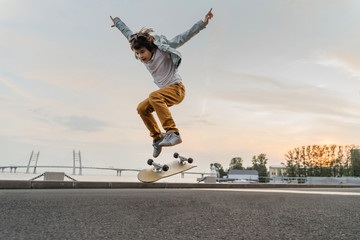 Boy jumping on skateboard at the street. Funny kid skater practicing ollie on skateboard at sunset. - obrazy, fototapety, plakaty