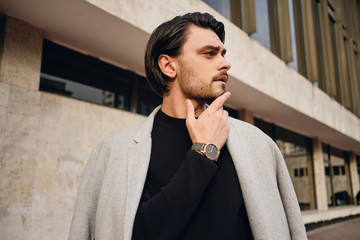 Side view of young wistful man with coat on shoulders thoughtfully looking away outdoor