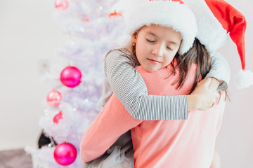 Loving mother and daughter hugging near christmas tree, looking amazing.