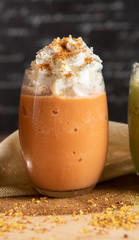 Thai tea smoothie, decorate topping with whipping cream in a clear glass on a chopper with dark gray real wood floor. Popular drink to quench thirst to cool down. Thai tea leaf and powder in front.