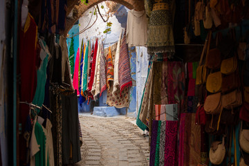 Fototapeta na wymiar Narrow streets and blue painted houses of Chefchaouen city, Morocco. Most of the streets full of handmade colorful crafts,carpets and souvenir hanged to the walls of the blue houses.
