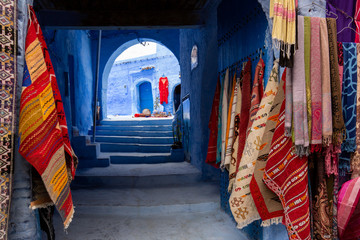 Narrow streets and blue painted houses of Chefchaouen city, Morocco. Most of the streets full of handmade colorful crafts,carpets and souvenir hanged to the walls of the blue houses.