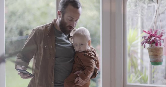 Single parent working from home on smart phone and holding baby