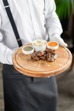 The waiter is holding a plate Pieces of liver cooked on the grill. Serving on a wooden Board. Barbecue restaurant menu, a series of photos of different meats. Pickled cabbage and two sauces