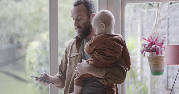 Single parent working from home on smart phone and holding baby