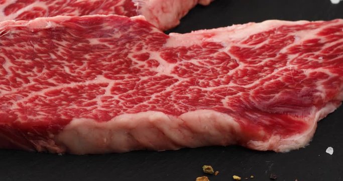 Fresh raw beef meat Denver Steak with peppercorns, seasonings and spices, ready to grill, rotating 360. Front view